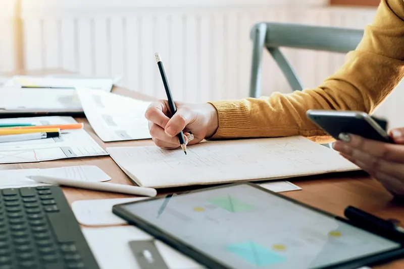 Aan welke eisen moet een factuur voldoen? Ondernemer controleert facturen en bonnen aan een bureau met laptop en tablet